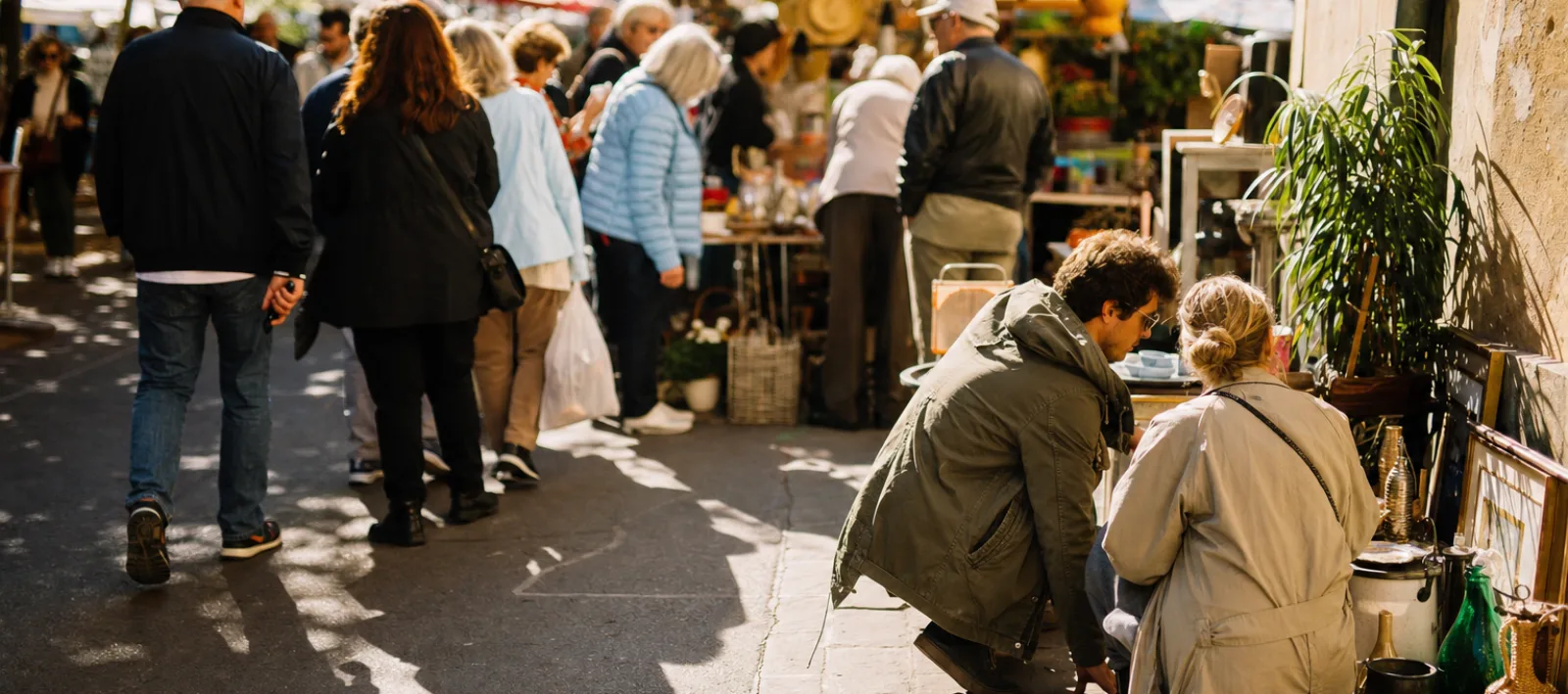 Shoppers crowd a busy market stall while two people examine an unusual stall at the edge